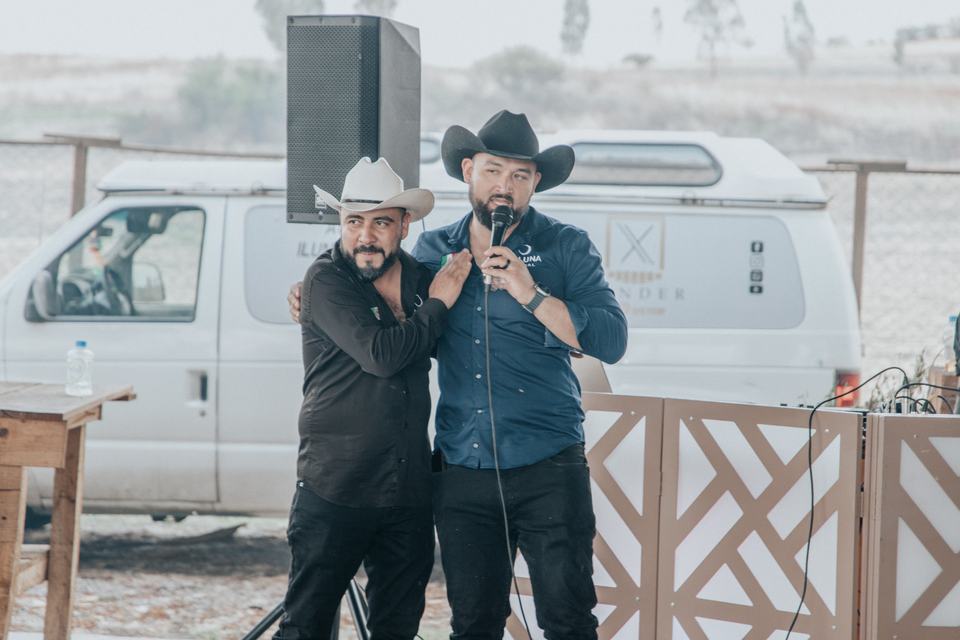 Salvador and Adrian arm in arm at a microphone, speaking to a gathering outdoors.